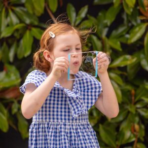 Tiger Tribe Bubble-ology - Lifestyle shot of a girl blowing a large bubble between two straws connected by white string