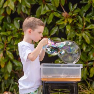 Tiger Tribe Bubble-ology - Lifestyle shot of a boy blowing a large bubble between two straws connected by white string