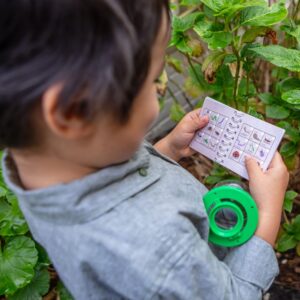 Tiger Tribe Bug Spotter Kit - Lifestyle shot with boy reading handbook and holding magnifying Bug Spotter
