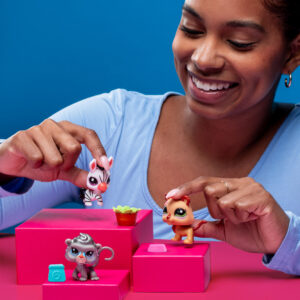 A person with a joyful expression is playing with three toy animals on pink blocks against a blue background. The toys include a zebra, a lion, and a monkey. The person, wearing a light blue top, holds the zebra and lion toys.