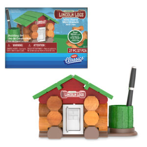 A Lincoln Logs building set is shown with a small, log cabin-style house made from the logs. The cabin has a white door, red Lincoln Logs sign, and a green roof. A green base serves as a pen holder with a pen beside the house. Packaging includes product details.