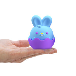 A blue and purple toy bunny sits in a person's hand. The bunny has features like closed eyes with upward curves, a yellow nose, and short, round ears. The bunny is partially enclosed in a purple shell. The background is white.