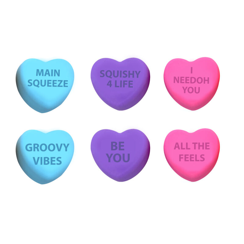 Six heart-shaped sensory toys arranged in two rows. The top row has blue, purple, and pink hearts labeled "MAIN SQUEEZE", "SQUISHY 4 LIFE", and "I NEEDOH YOU". The bottom row has blue, purple, and pink hearts labeled "GROOVY VIBES", "BE YOU", and "ALL THE FEELS".