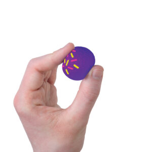 A hand holding a small, round tan ball against a plain white background. The ball looks like a donut hole with sprinkles and is being squeezed. You can see a white filling inside through the material.