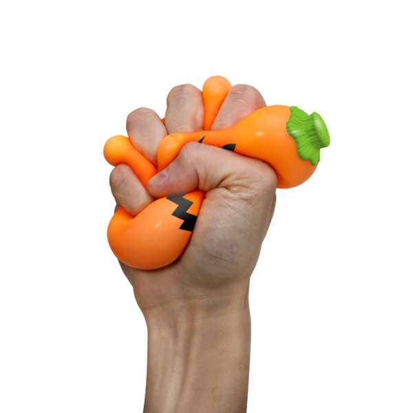 A hand is squeezing a NeeDoh Jack-Glow-Lantern on a white background. The toy is squishing through the fingers of the hand, showing its soft, squeezy nature.