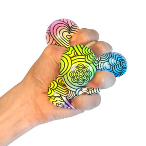 A hand squeezing a NeeDoh Press-Doh. The colorful doh is visible through the white and black designs of the exterior.