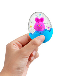 A hand is holding a small, clear, egg-shaped snow globe like squishy toy with a blue base. Inside the globe is a pink bunny with a smiling face and colorful stars floating around it. The background is plain white.