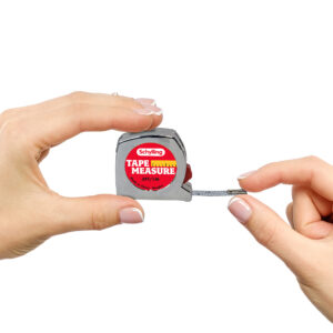 Two hands holding a miniature tape measure with a metallic body. The tape measure, branded "Schylling," has a partially extended measuring tape displaying centimeter and inch marks. The text on the tape measure reads "Tape Measure" and 3ft/1M.