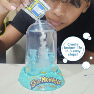 A child wearing a dark shirt and pink nailpolish is bent over the aquarium, and pouring powder into it from a small packet labeled with the number 1. There is a callout in a circle that reads "Create instant life in 3 easy steps!".