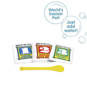 Three packets, numbered 1, 2, and 3 from left to right. There is a small yellow Sea-Monkeys spoon laying in front of the packets. There are two callouts in circles. One reads "World's Easiest Pet!" and the other reads "Just add water!"